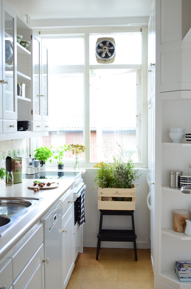 This is an example of a scandinavian galley kitchen in Copenhagen with a drop-in sink, raised-panel cabinets, white cabinets, beige splashback, white appliances and brown floor.