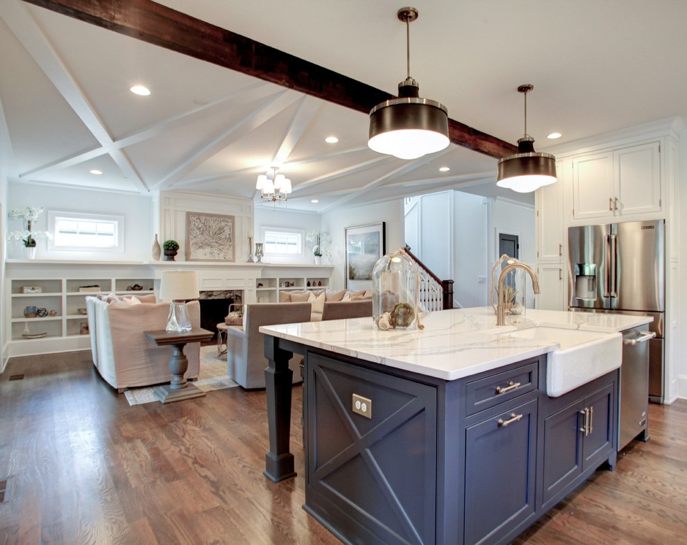 Photo of a mid-sized arts and crafts single-wall open plan kitchen in Atlanta with a farmhouse sink, glass-front cabinets, white cabinets, marble benchtops, white splashback, marble splashback, stainless steel appliances, medium hardwood floors, with island and beige floor.