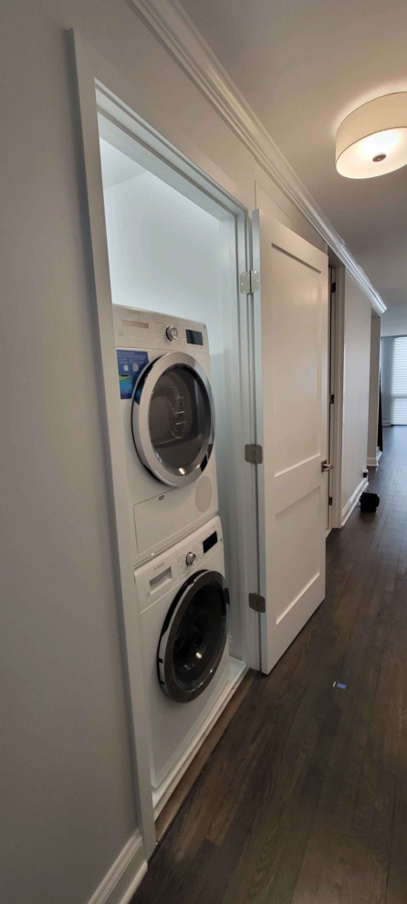 Kleine Moderne Waschküche mit flächenbündigen Schrankfronten, weißer Wandfarbe, Porzellan-Bodenfliesen, Waschmaschine und Trockner gestapelt und weißem Boden in Chicago