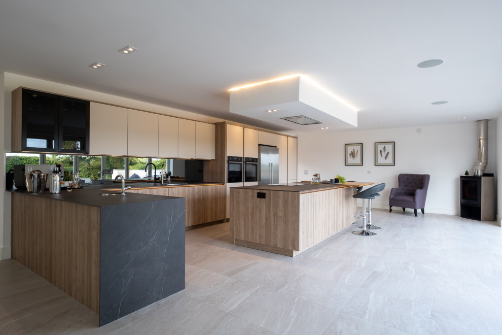 Large contemporary l-shaped open plan kitchen in Hampshire with flat-panel cabinets, white cabinets, grey splashback, glass sheet splashback, porcelain floors, with island, multi-coloured floor and grey benchtop.