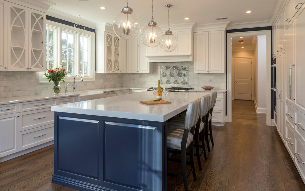 Inspiration for a large transitional u-shaped medium tone wood floor and brown floor eat-in kitchen remodel in New York with a farmhouse sink, white cabinets, granite countertops, gray backsplash, ceramic backsplash, stainless steel appliances, an island and white countertops