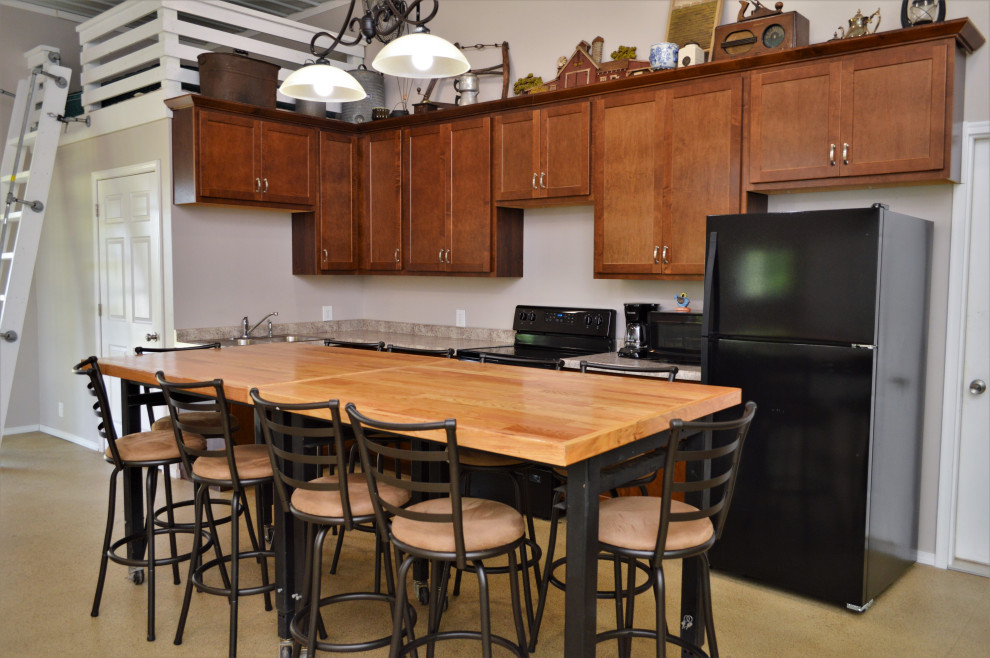 Mid-sized transitional l-shaped cement tile floor and yellow floor open concept kitchen photo with a drop-in sink, shaker cabinets, brown cabinets, wood countertops, brown backsplash, black appliances, an island and brown countertops
