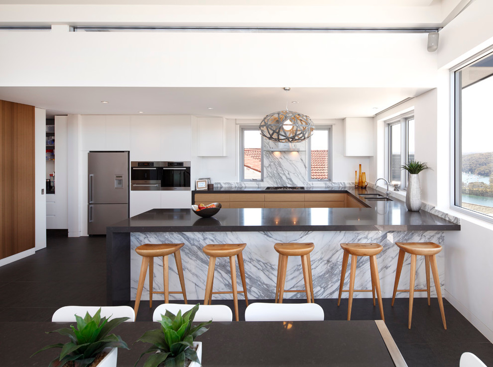 This is an example of a contemporary u-shaped open plan kitchen in Sydney with flat-panel cabinets, white splashback, stone slab splashback and a peninsula.