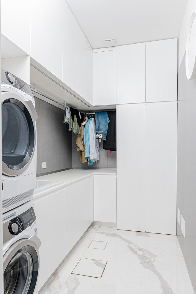 Contemporary single-wall dedicated laundry room in Other with an utility sink, flat-panel cabinets, white cabinets, wood benchtops, grey splashback, porcelain splashback, grey walls, porcelain floors, a stacked washer and dryer, white floor and white benchtop.