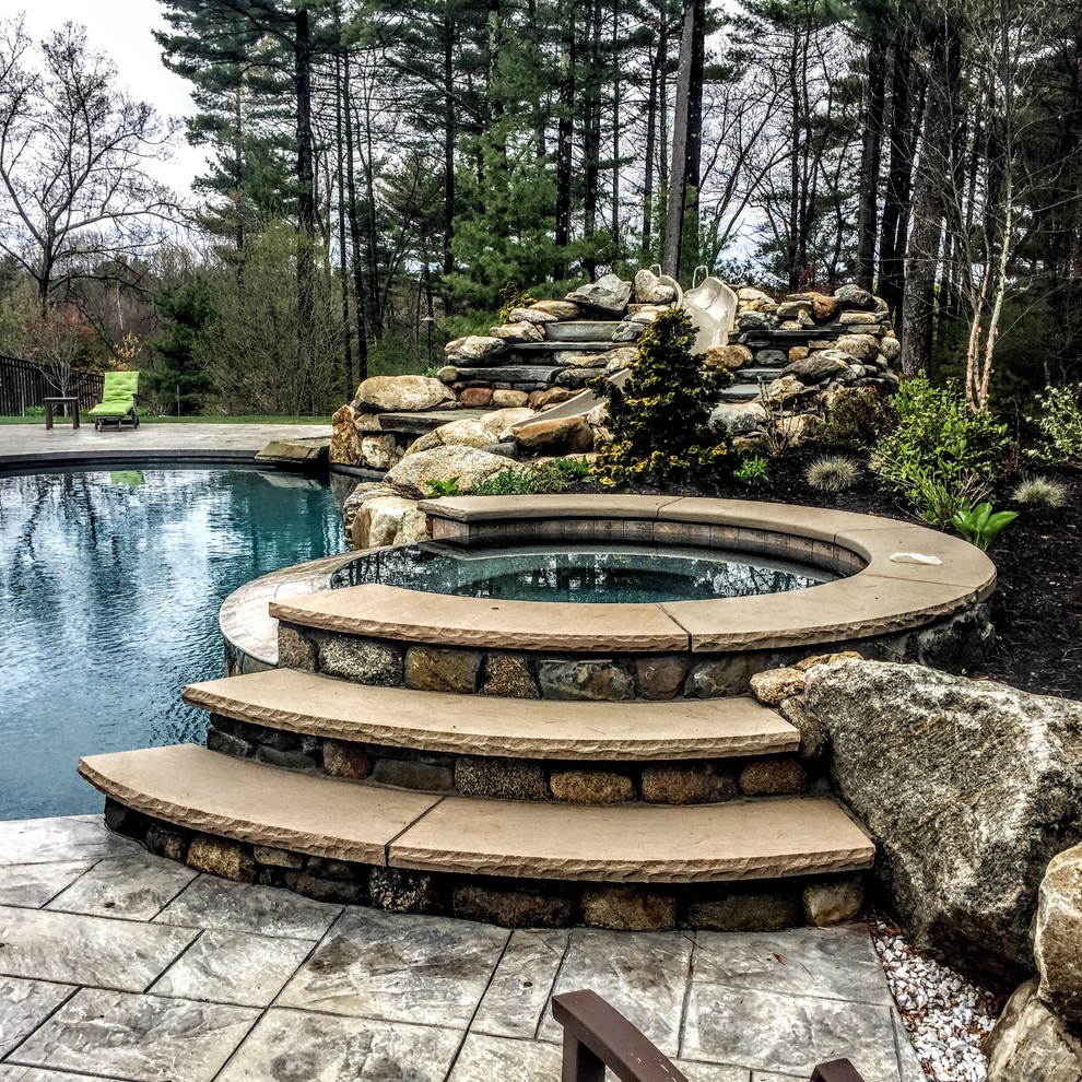 This is an example of a mid-sized traditional backyard custom-shaped natural pool in Boston with a hot tub and stamped concrete.