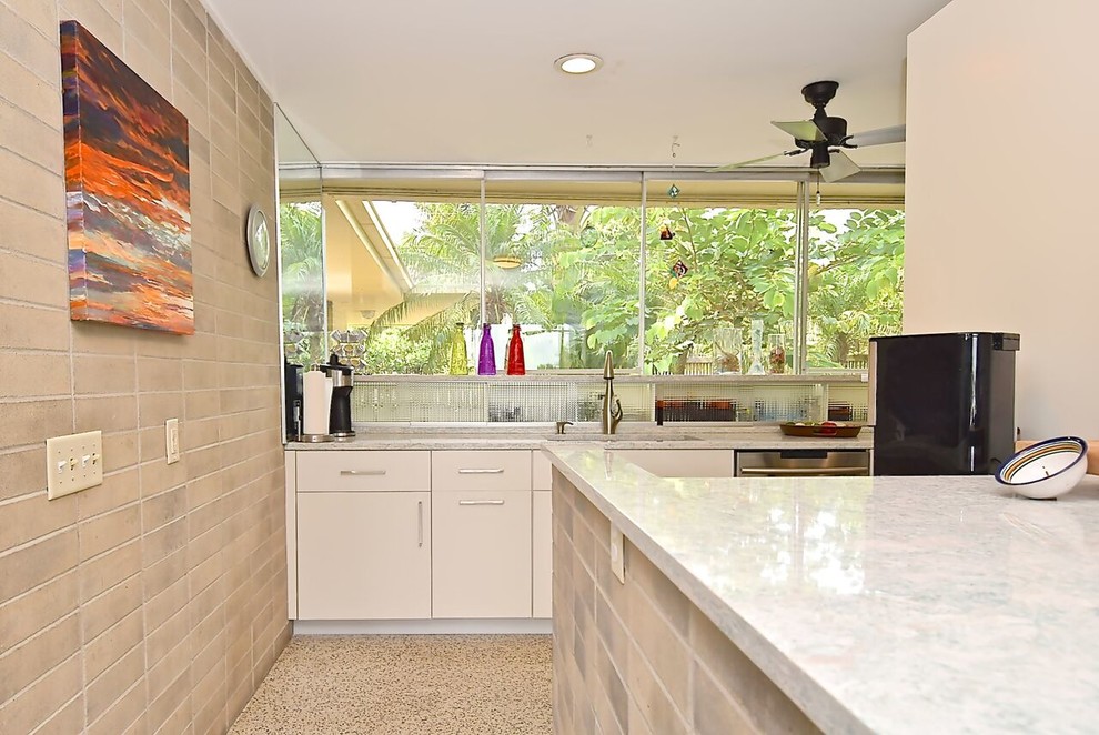 Photo of a large midcentury galley open plan kitchen in Other with an integrated sink, flat-panel cabinets, white cabinets, quartz benchtops, grey splashback, stainless steel appliances, terrazzo floors, with island, white floor and white benchtop.