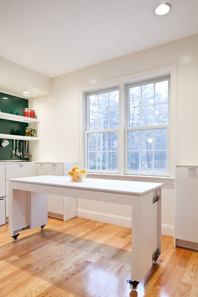 Design ideas for a contemporary u-shaped eat-in kitchen in Boston with an undermount sink, flat-panel cabinets, white cabinets, solid surface benchtops, green splashback, glass sheet splashback and stainless steel appliances.