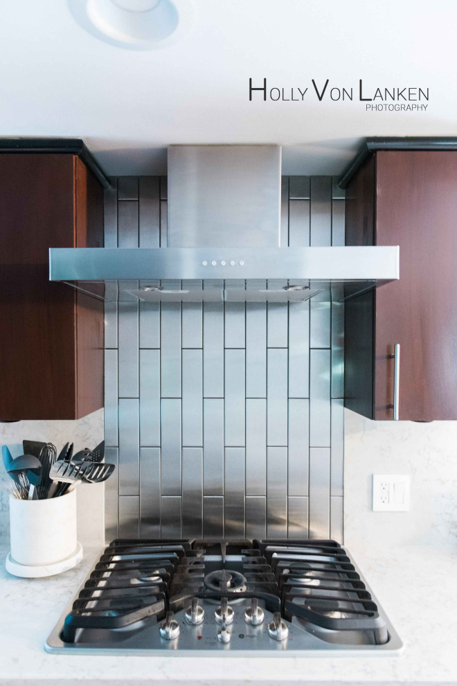 This is an example of a modern eat-in kitchen in Indianapolis with metal splashback, stainless steel appliances, white benchtop, flat-panel cabinets, metallic splashback, dark wood cabinets and light hardwood floors.
