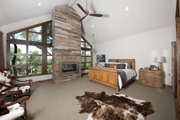 This is an example of a large country master bedroom in Austin with white walls, carpet, a two-sided fireplace, a wood fireplace surround and grey floor.