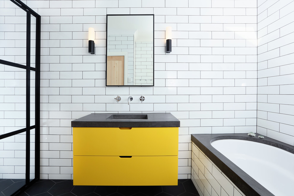 Mid-sized contemporary kids bathroom in Melbourne with flat-panel cabinets, yellow cabinets, white tile, subway tile, white walls, an undermount sink, concrete benchtops, black floor, grey benchtops, an undermount tub, porcelain floors, a single vanity, a floating vanity, brick walls, an alcove shower and a sliding shower screen.