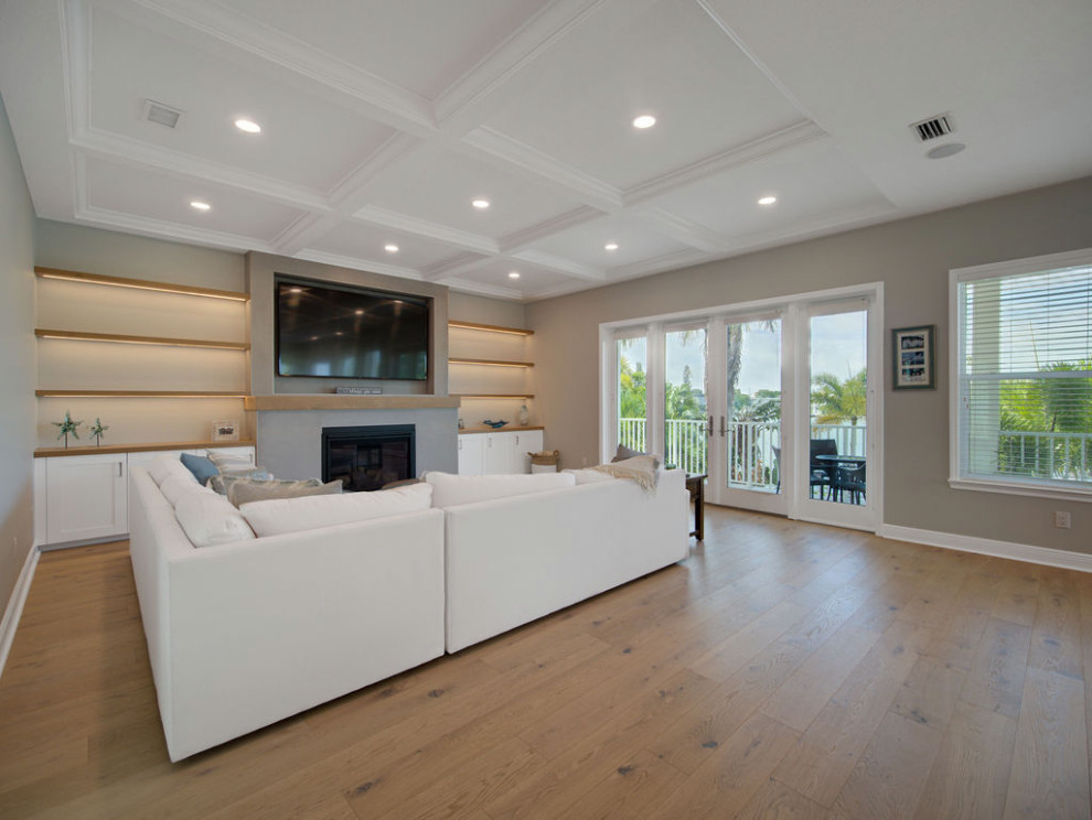 Example of a large beach style open concept medium tone wood floor, brown floor and coffered ceiling family room design in Tampa with beige walls, a standard fireplace, a tile fireplace and a media wall