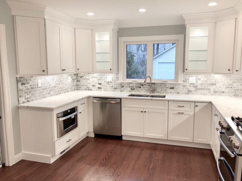 Mid-sized transitional u-shaped dark wood floor and brown floor enclosed kitchen photo with an undermount sink, shaker cabinets, white cabinets, marble countertops, gray backsplash, stone tile backsplash, stainless steel appliances, no island and white countertops