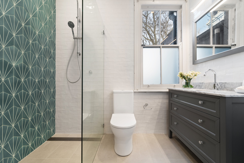 This is an example of a transitional 3/4 bathroom in Sydney with recessed-panel cabinets, grey cabinets, a curbless shower, a two-piece toilet, green tile, white tile, subway tile, an undermount sink, marble benchtops, beige floor and grey benchtops.