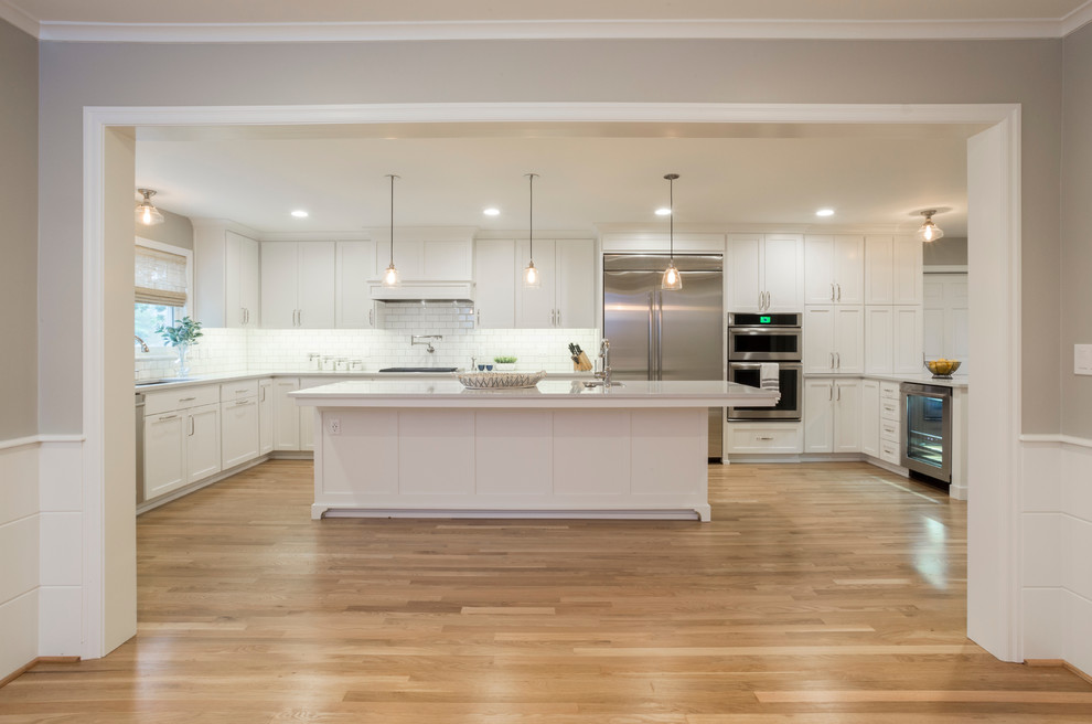 This is an example of a large transitional u-shaped separate kitchen in Portland with an undermount sink, shaker cabinets, white cabinets, quartzite benchtops, white splashback, subway tile splashback, stainless steel appliances, light hardwood floors, with island, brown floor and white benchtop.