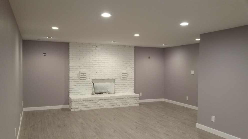 This is an example of a large transitional look-out basement in Edmonton with purple walls, laminate floors, a standard fireplace, a brick fireplace surround and grey floor.