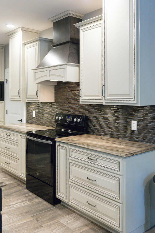 Example of a large transitional l-shaped ceramic tile eat-in kitchen design in Chicago with an undermount sink, raised-panel cabinets, dark wood cabinets, marble countertops, brown backsplash, glass tile backsplash, black appliances and an island