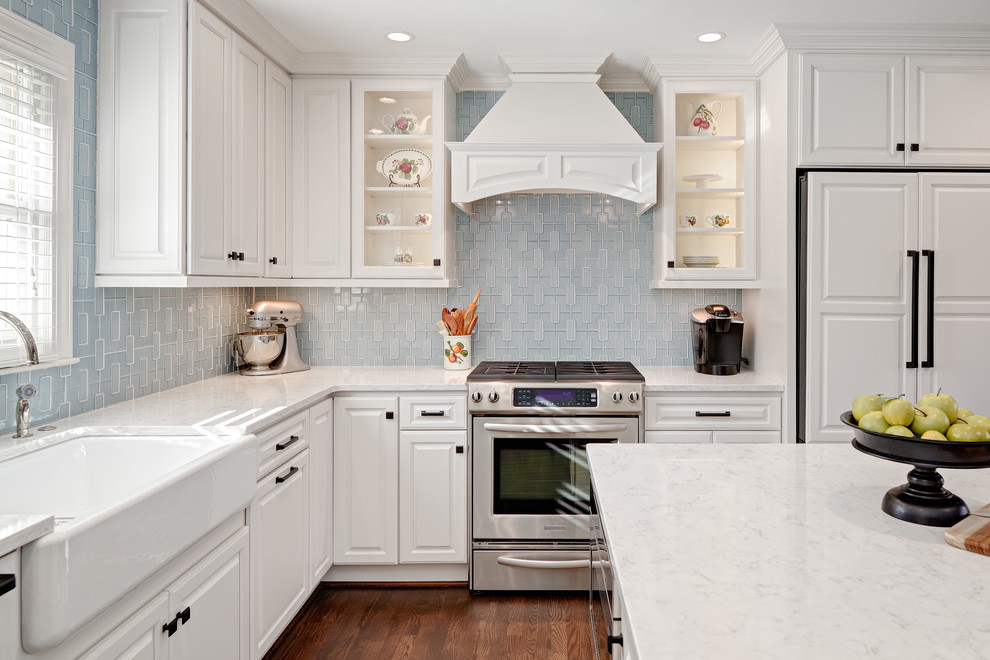 Mid-sized transitional u-shaped medium tone wood floor and brown floor eat-in kitchen photo with a farmhouse sink, raised-panel cabinets, white cabinets, quartz countertops, blue backsplash, porcelain backsplash, paneled appliances and an island