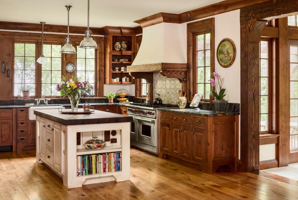Large traditional l-shaped kitchen in Milwaukee with marble benchtops, ceramic splashback, stainless steel appliances, medium hardwood floors, with island, raised-panel cabinets, dark wood cabinets and brown floor.