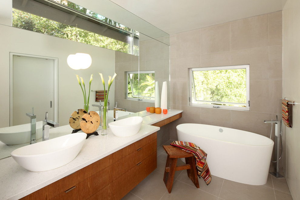 This is an example of a mid-sized modern master bathroom in Los Angeles with a vessel sink, flat-panel cabinets, medium wood cabinets, a freestanding tub, beige tile, stone tile, beige walls, porcelain floors, engineered quartz benchtops, beige floor and white benchtops.