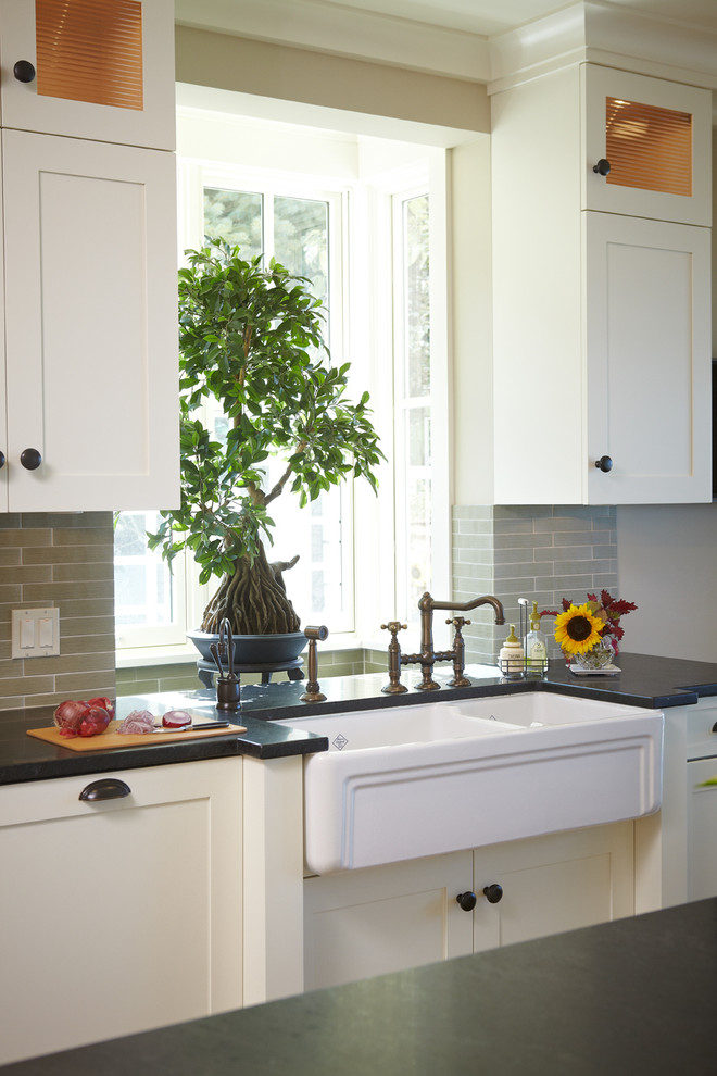 Eat-in kitchen - mid-sized transitional galley medium tone wood floor and brown floor eat-in kitchen idea in Grand Rapids with a farmhouse sink, shaker cabinets, white cabinets, soapstone countertops, gray backsplash, matchstick tile backsplash, stainless steel appliances and an island