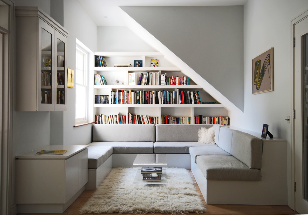 Contemporary enclosed living room in London with a library, white walls, light hardwood floors and no tv.