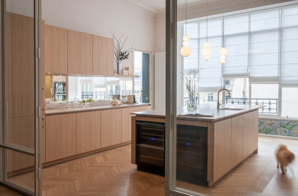 Inspiration for a large contemporary galley separate kitchen in Paris with a single-bowl sink, light wood cabinets, marble benchtops, white splashback, marble splashback, black appliances, light hardwood floors, with island, white benchtop, flat-panel cabinets and beige floor.