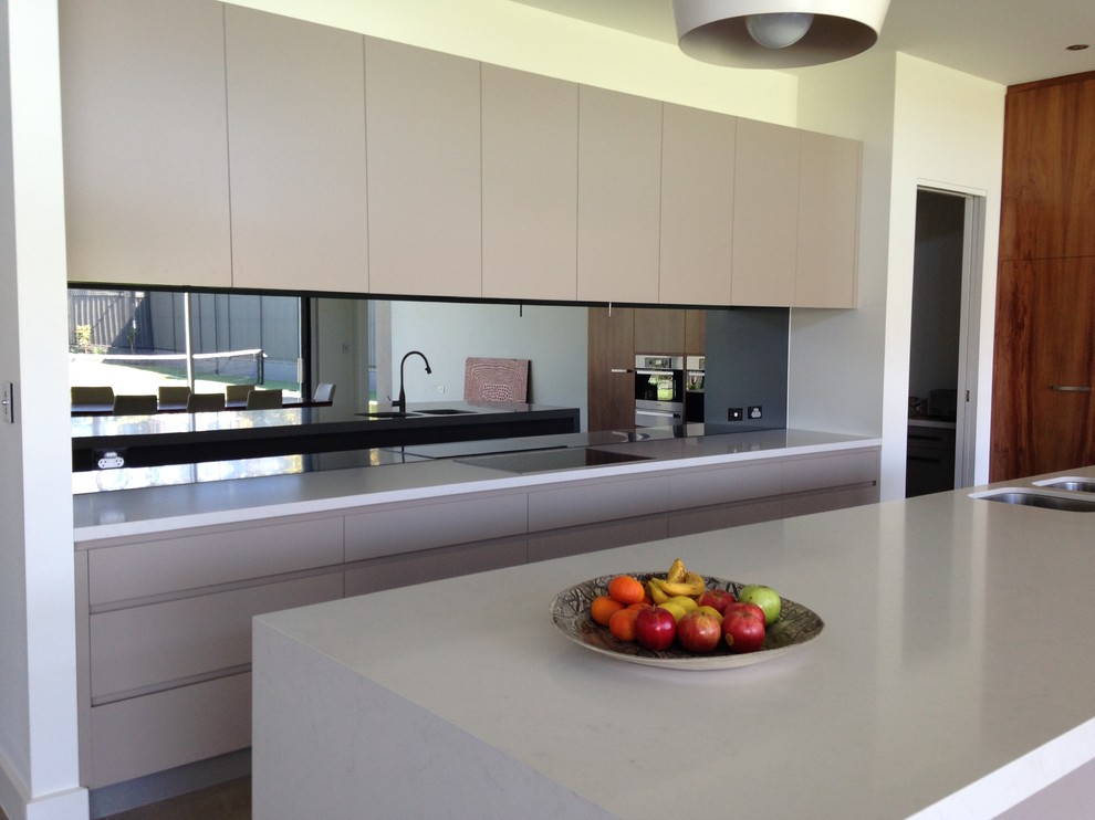 Photo of a contemporary kitchen in Adelaide with an undermount sink, flat-panel cabinets, beige cabinets, solid surface benchtops, mirror splashback, panelled appliances and with island.