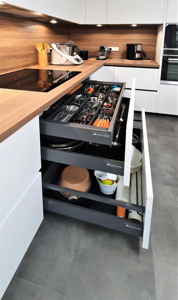 This is an example of a large contemporary l-shaped open plan kitchen in Other with a submerged sink, flat-panel cabinets, white cabinets, wood worktops, brown splashback, wood splashback, integrated appliances, concrete flooring, an island, grey floors and brown worktops.