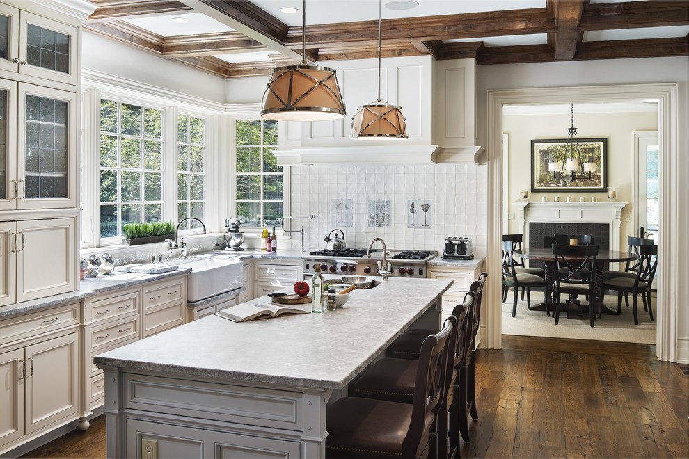 This is an example of a traditional l-shaped kitchen in New York with a farmhouse sink, beaded inset cabinets, white cabinets, white splashback, stainless steel appliances, medium hardwood floors and with island.