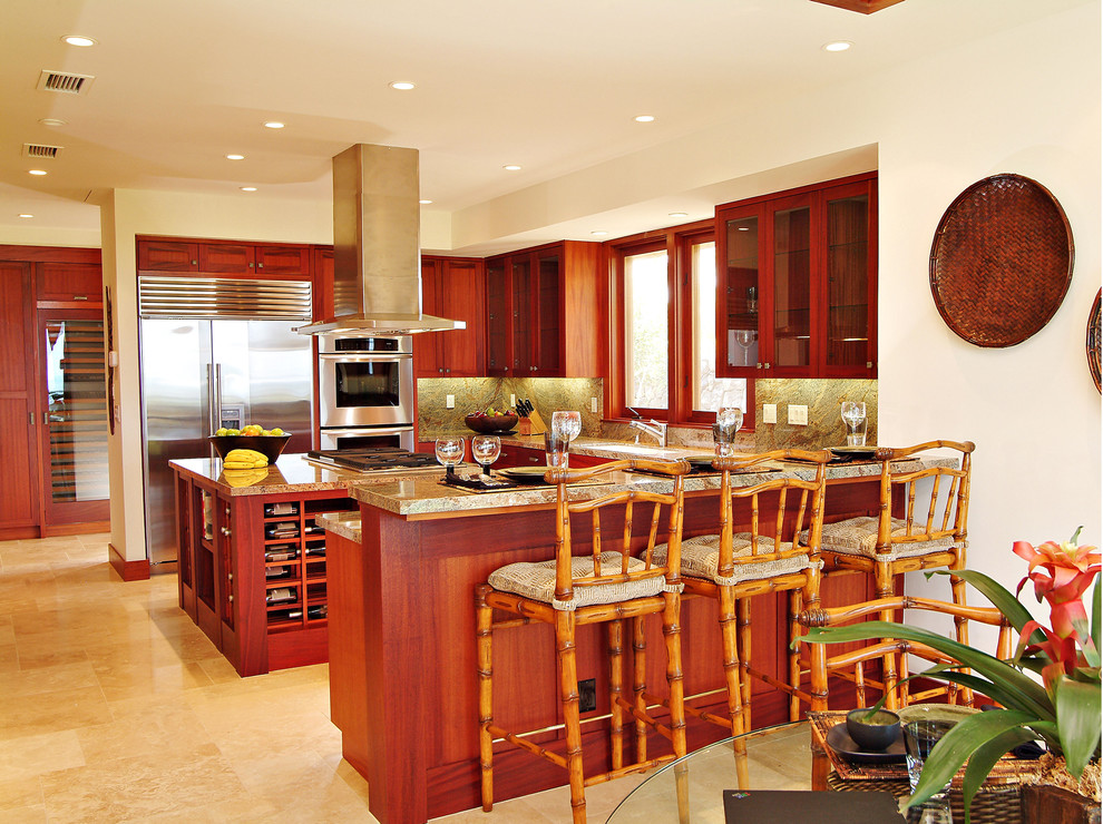 This is an example of a large tropical u-shaped eat-in kitchen in Hawaii with shaker cabinets, medium wood cabinets, granite benchtops, beige splashback, stone slab splashback, stainless steel appliances, travertine floors, with island, beige floor and beige benchtop.
