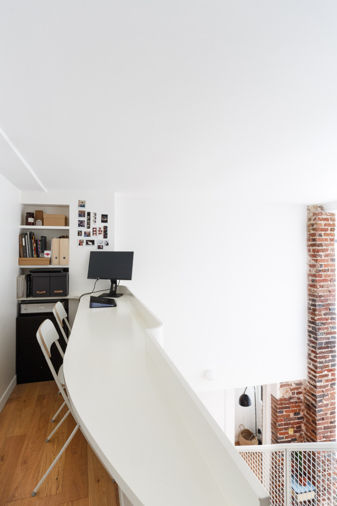 Diseño de despacho industrial pequeño sin chimenea con paredes blancas, suelo de madera en tonos medios, escritorio empotrado y suelo marrón