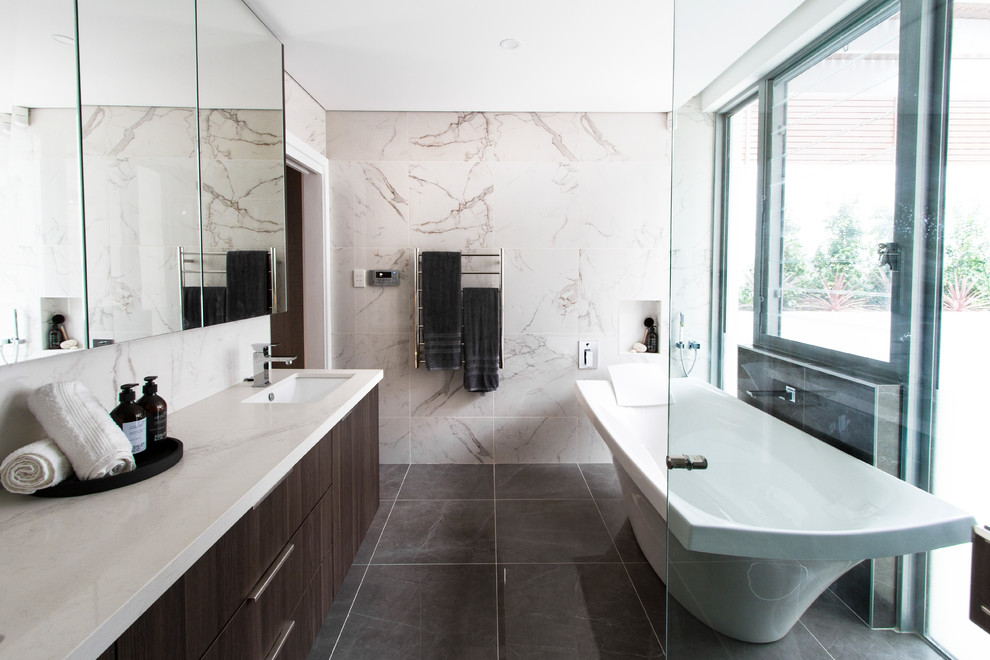 This is an example of a large contemporary master bathroom in Sydney with flat-panel cabinets, white cabinets, a freestanding tub, brown walls, ceramic floors, a drop-in sink, a double shower, a one-piece toilet, marble, marble benchtops, black floor and a hinged shower door.