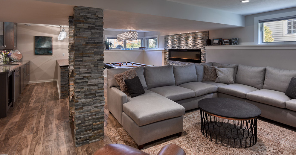 Example of a mid-sized transitional look-out vinyl floor and brown floor basement design with gray walls, a ribbon fireplace and a stone fireplace