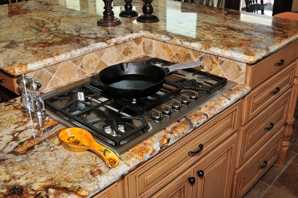 Example of a large transitional l-shaped porcelain tile and brown floor eat-in kitchen design in Houston with a double-bowl sink, raised-panel cabinets, medium tone wood cabinets, granite countertops, beige backsplash, travertine backsplash, stainless steel appliances and an island