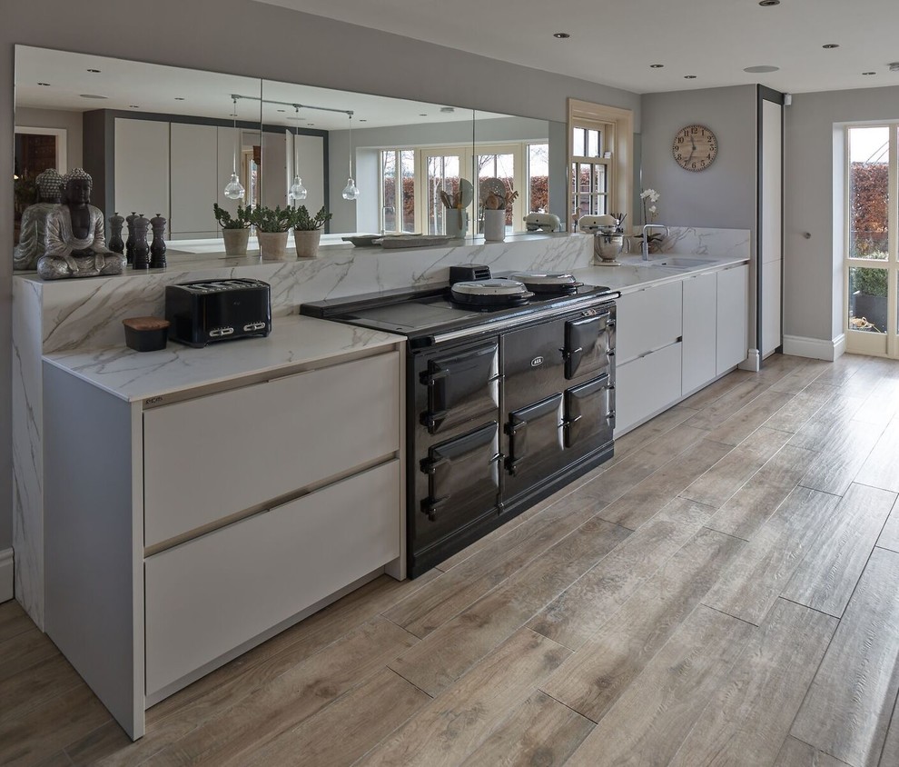 Large contemporary galley eat-in kitchen in Other with an integrated sink, flat-panel cabinets, white cabinets, solid surface benchtops, metallic splashback, mirror splashback, black appliances, medium hardwood floors, with island and brown floor.