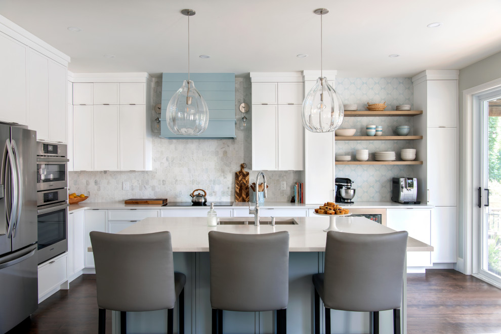 Example of a transitional u-shaped medium tone wood floor and brown floor kitchen design in Ottawa with an undermount sink, shaker cabinets, white cabinets, quartz countertops, multicolored backsplash, stainless steel appliances, an island and beige countertops