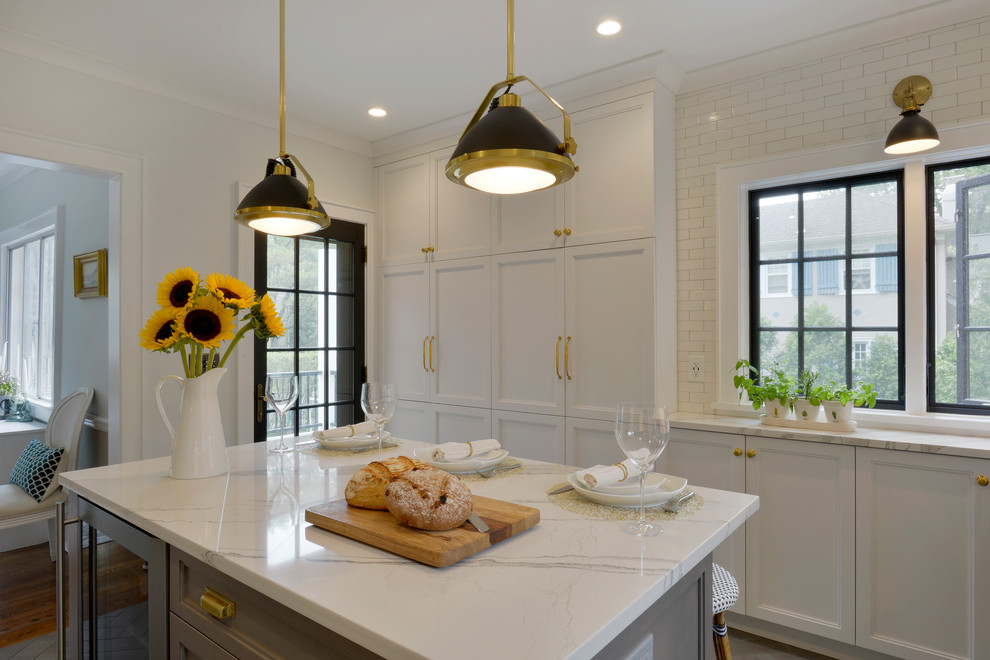 This is an example of a small transitional u-shaped separate kitchen in New York with an undermount sink, recessed-panel cabinets, white cabinets, quartz benchtops, white splashback, ceramic splashback, stainless steel appliances, porcelain floors, with island, grey floor and white benchtop.