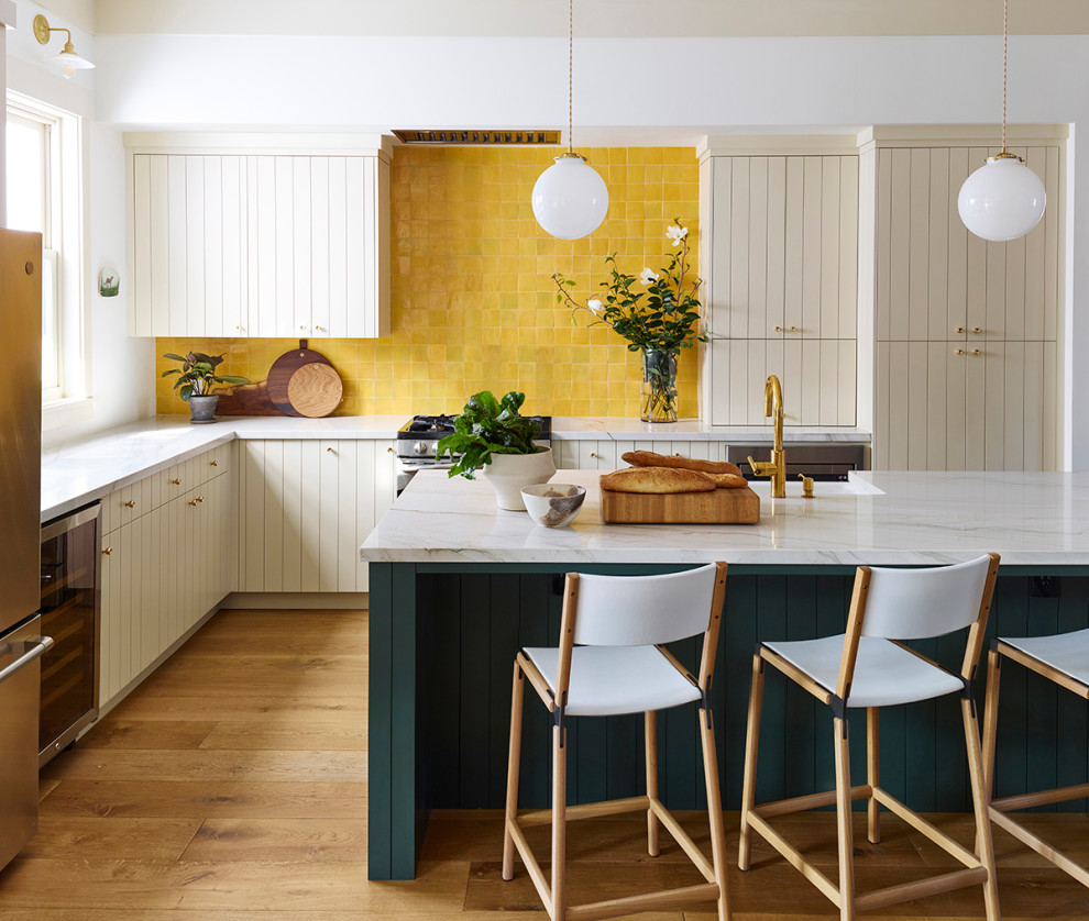 Mid-sized country l-shaped open plan kitchen in San Francisco with a farmhouse sink, flat-panel cabinets, white cabinets, quartzite benchtops, yellow splashback, terra-cotta splashback, stainless steel appliances, medium hardwood floors, with island and white benchtop.