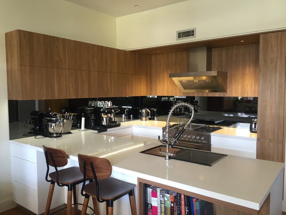 Mid-sized modern u-shaped eat-in kitchen in Sydney with a double-bowl sink, shaker cabinets, medium wood cabinets, solid surface benchtops, black splashback, mirror splashback, stainless steel appliances, medium hardwood floors and with island.