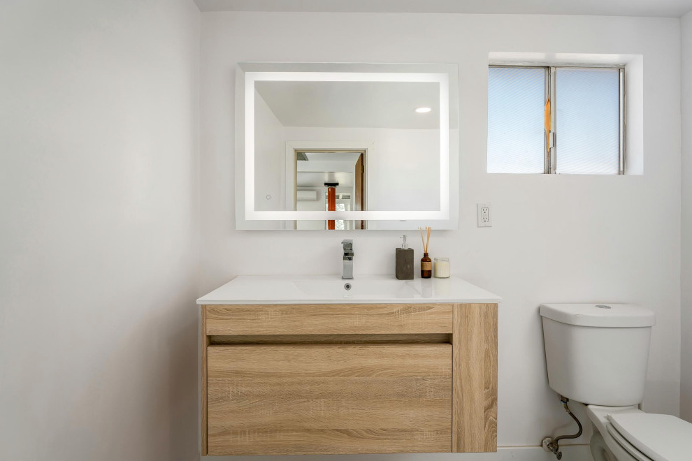 Источник вдохновения для домашнего уюта: маленькая ванная комната в стиле модернизм с плоскими фасадами, светлыми деревянными фасадами, душем в нише, раздельным унитазом, белой плиткой, белыми стенами, бетонным полом, душевой кабиной, монолитной раковиной, столешницей из искусственного камня, бежевым полом, душем с распашными дверями, белой столешницей, тумбой под одну раковину и подвесной тумбой для на участке и в саду