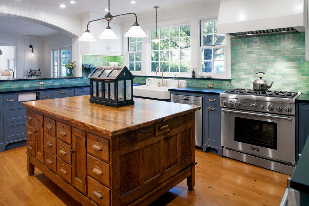 Photo of a mid-sized country u-shaped eat-in kitchen in Los Angeles with a farmhouse sink, shaker cabinets, grey cabinets, green splashback, ceramic splashback, stainless steel appliances, medium hardwood floors, with island and wood benchtops.