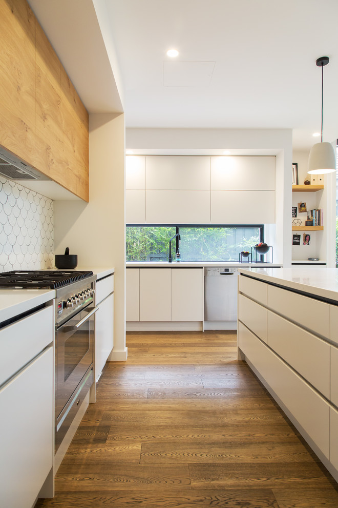 Photo of a mid-sized contemporary galley open plan kitchen in Melbourne with a drop-in sink, flat-panel cabinets, white cabinets, quartz benchtops, white splashback, ceramic splashback, stainless steel appliances, ceramic floors, with island, brown floor and white benchtop.