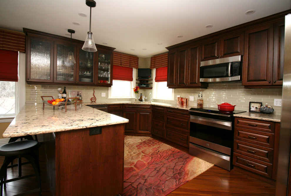 This is an example of a large traditional u-shaped eat-in kitchen in Other with an undermount sink, raised-panel cabinets, dark wood cabinets, quartz benchtops, beige splashback, glass tile splashback, stainless steel appliances, bamboo floors, a peninsula, brown floor and beige benchtop.