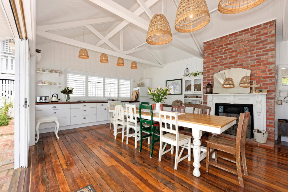 Tropical dining room in Brisbane with white walls, dark hardwood floors, a standard fireplace, brown floor and vaulted.
