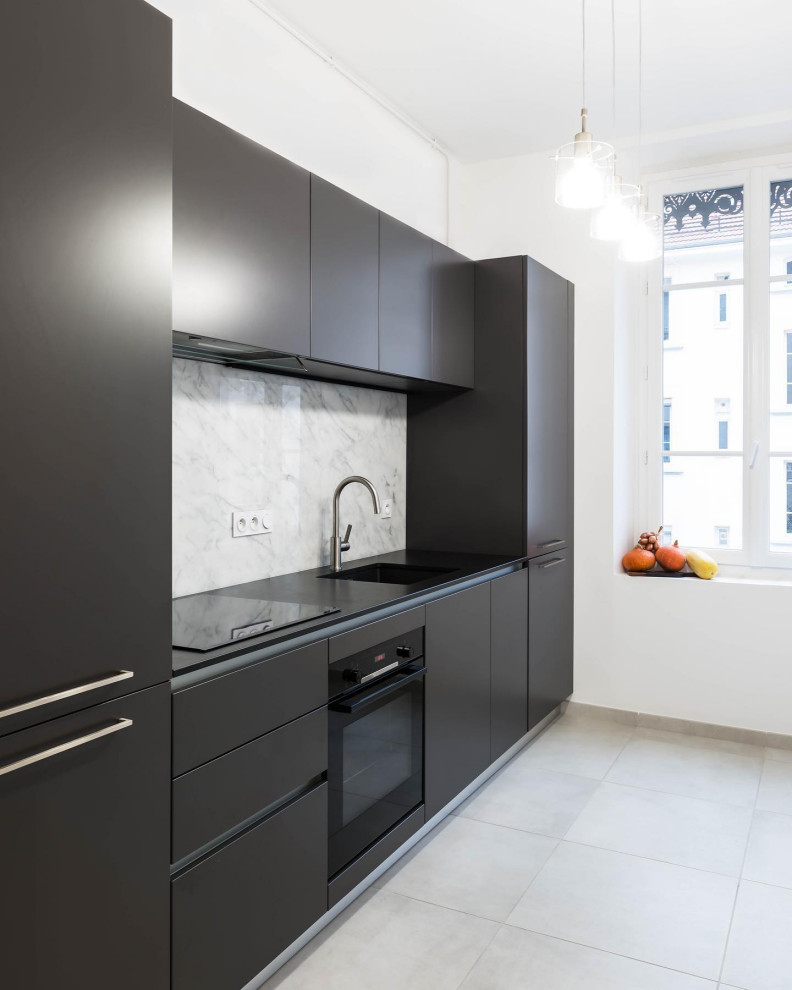 Small contemporary single-wall separate kitchen in Grenoble with an undermount sink, flat-panel cabinets, black cabinets, granite benchtops, white splashback, marble splashback, black appliances, no island, beige floor and black benchtop.