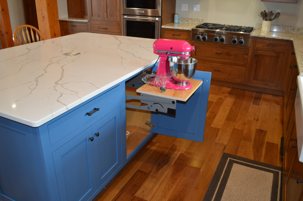 Example of a mid-sized mountain style u-shaped medium tone wood floor, brown floor and exposed beam eat-in kitchen design with a farmhouse sink, shaker cabinets, medium tone wood cabinets, paneled appliances and an island