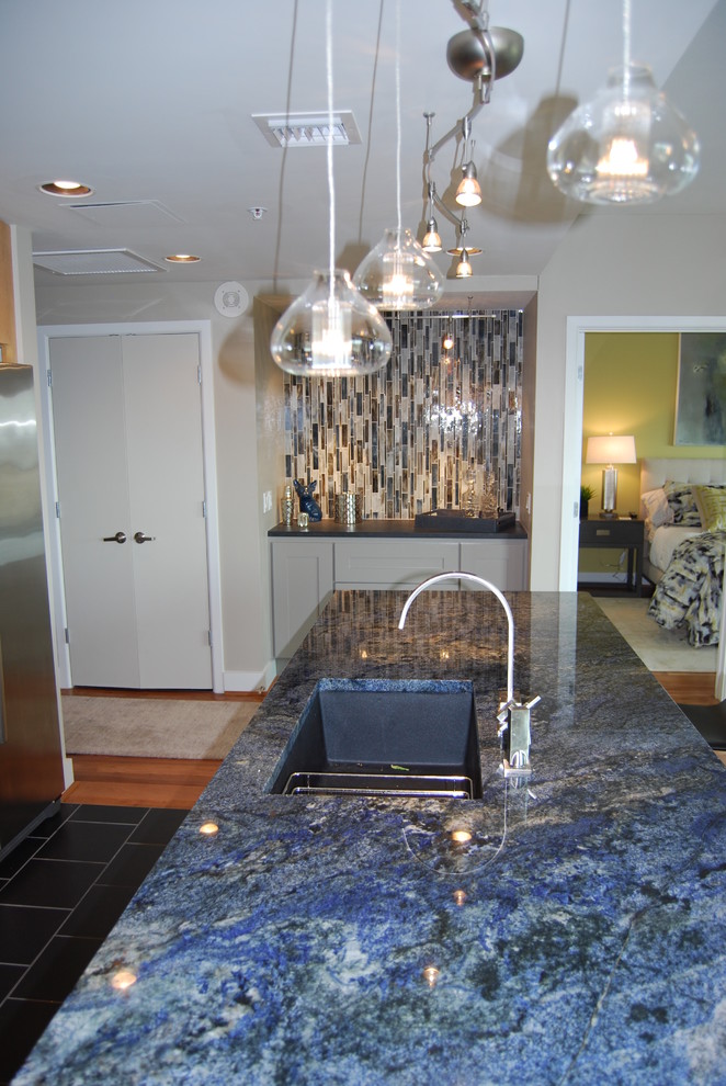 Example of a small transitional galley medium tone wood floor open concept kitchen design in Austin with an undermount sink, flat-panel cabinets, light wood cabinets, granite countertops, gray backsplash, porcelain backsplash, stainless steel appliances and an island