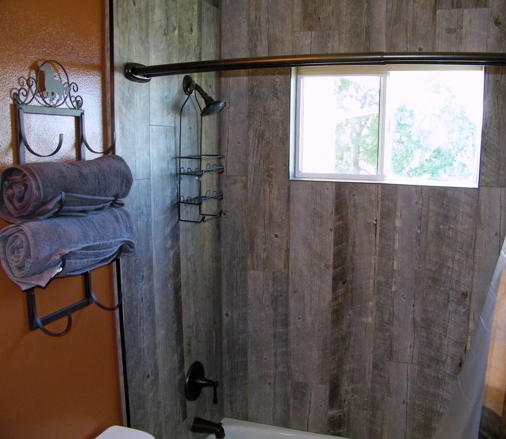 This is an example of a small country 3/4 bathroom in Sacramento with a drop-in tub, a shower/bathtub combo, a one-piece toilet, gray tile, porcelain tile, orange walls and porcelain floors.