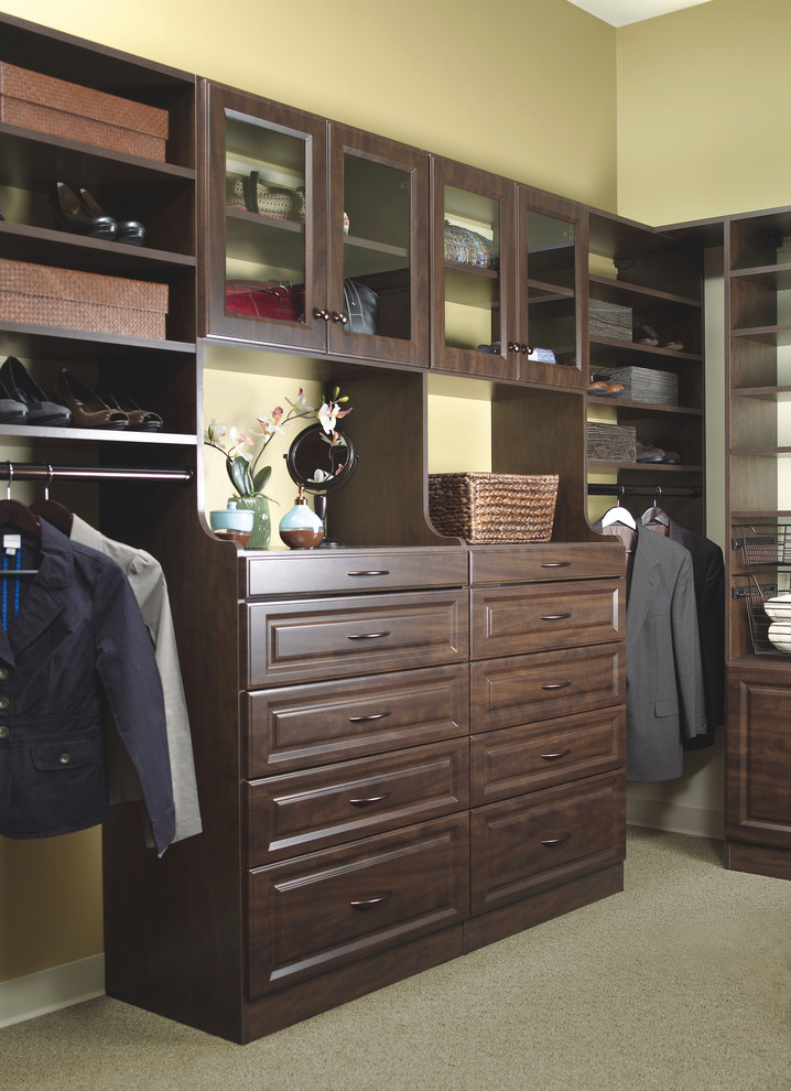 This is an example of a gender-neutral walk-in wardrobe in Philadelphia with glass-front cabinets, dark wood cabinets and carpet.