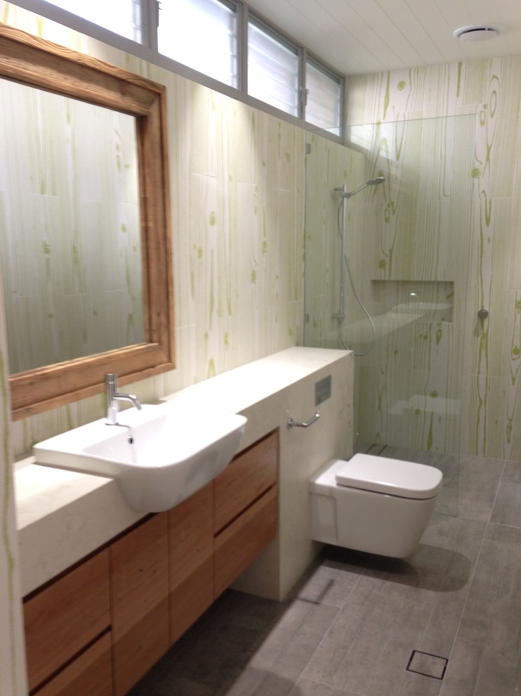 This is an example of a beach style kids bathroom in Sunshine Coast with a console sink, furniture-like cabinets, medium wood cabinets, limestone benchtops, a wall-mount toilet, green tile, porcelain tile, white walls and porcelain floors.